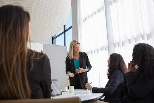 A business team in a modern office engaged in a presentation led by a woman, fostering teamwork and collaboration.